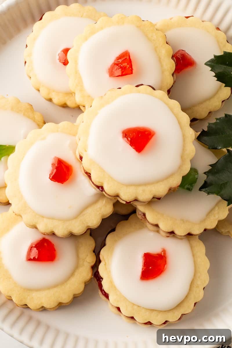 Overhead picture of empire cookies on a white plate with a sprig of fresh holly.