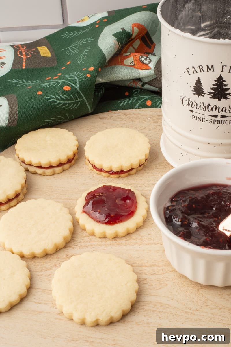 Empire cookies on cutting board being assembled with raspberry jam.