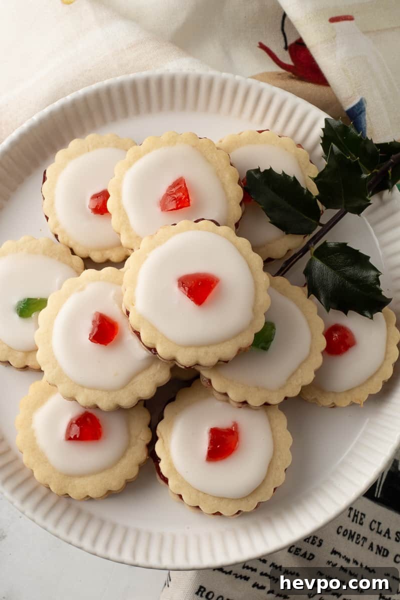 Empire cookies on white plate with fresh holly garnish.