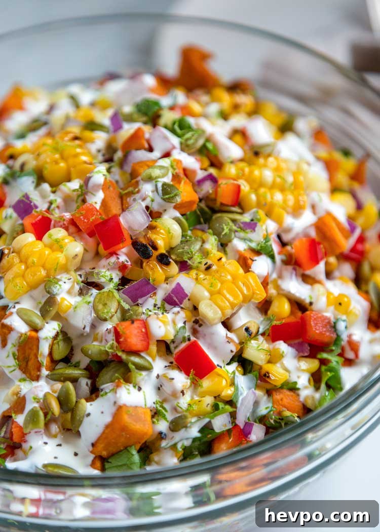This healthy Sweet Potato and Corn Salad has roasted sweet potatoes and corn, bell peppers and pumpkins seeds tossed in a Mexican crema sauce with lime. close up of Sweet Potato and Corn Salad in glass bowl