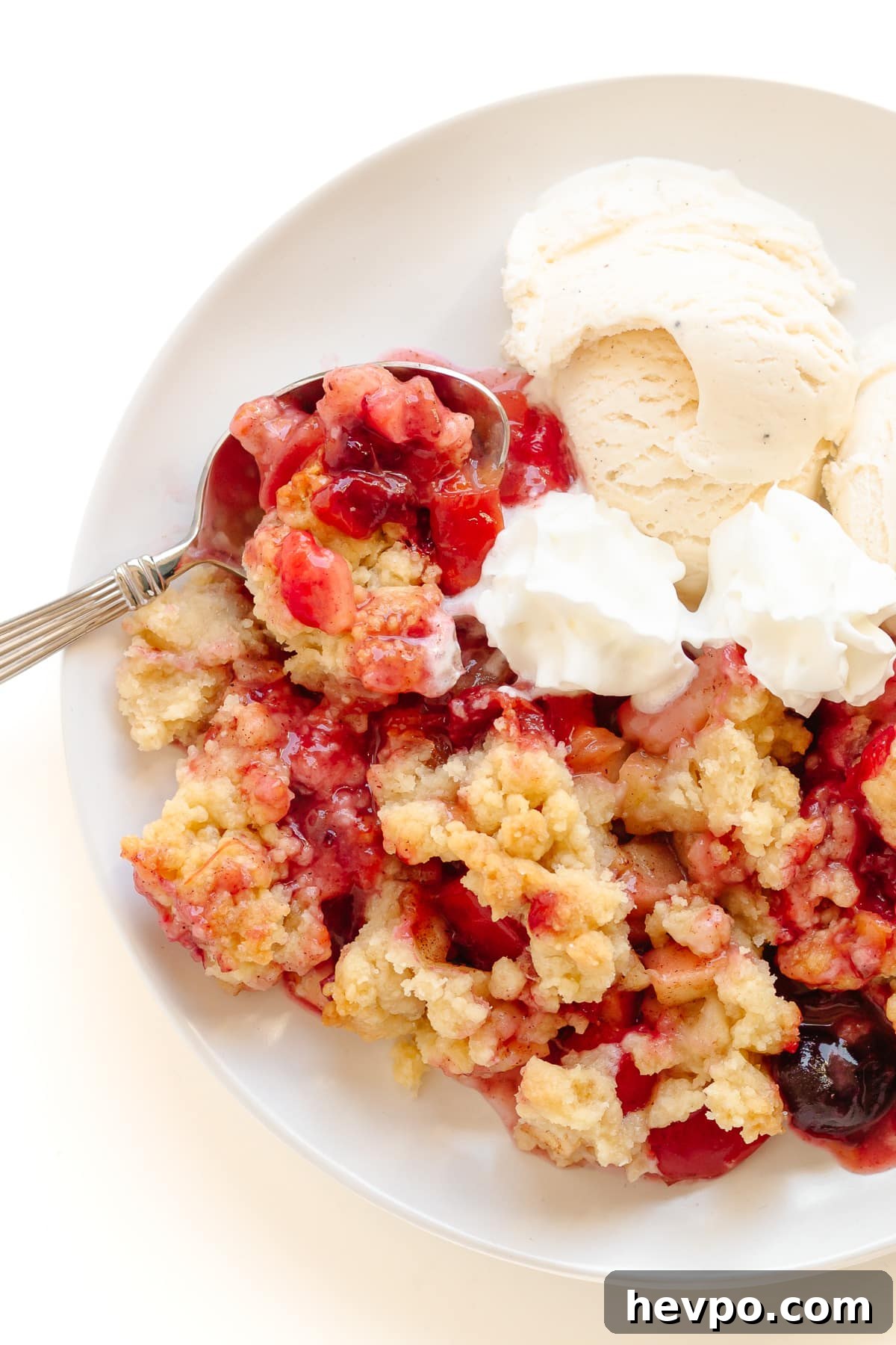 Plum and apple crumble on a plate served with vanilla ice cream and whipped cream.