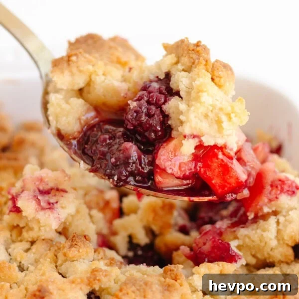 Serving spoon scooping up some apple and blackberry crumble from the baking dish.