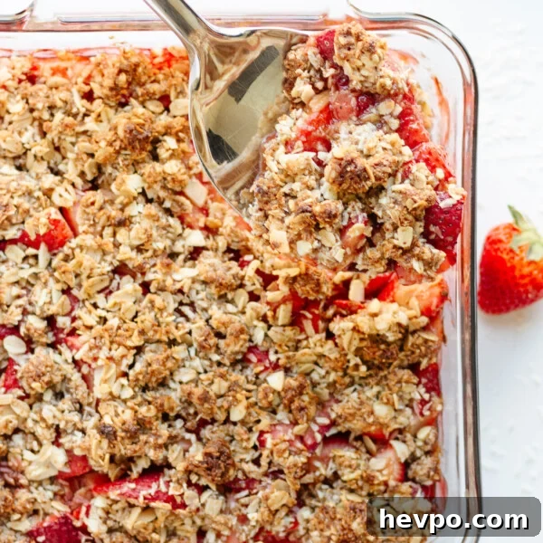 Serving spoon digging into a square glass dish of Strawberry Coconut Crisp.