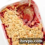Plum and apple crumble in a white baking dish with a portion scooped out.