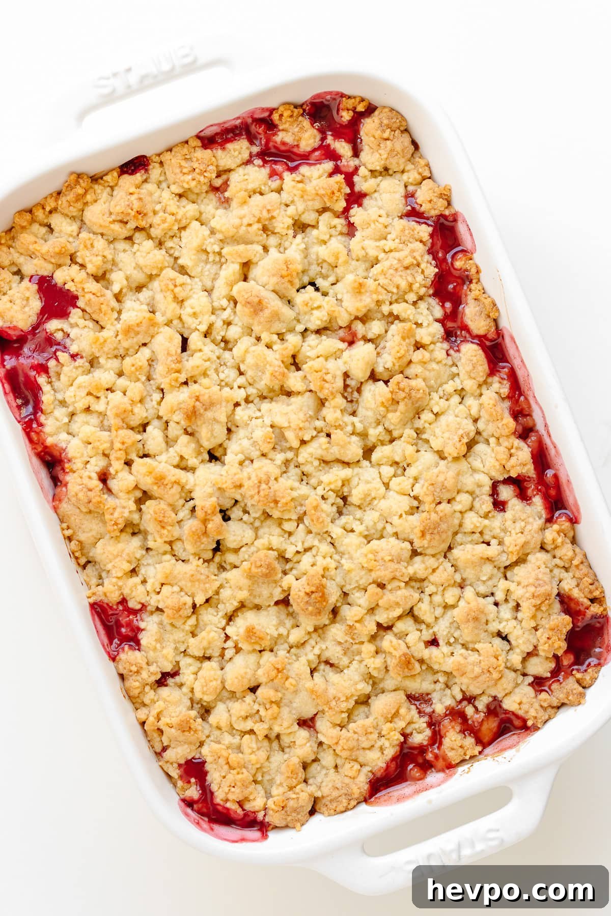 A baked plum and apple crumble in a white baking dish.