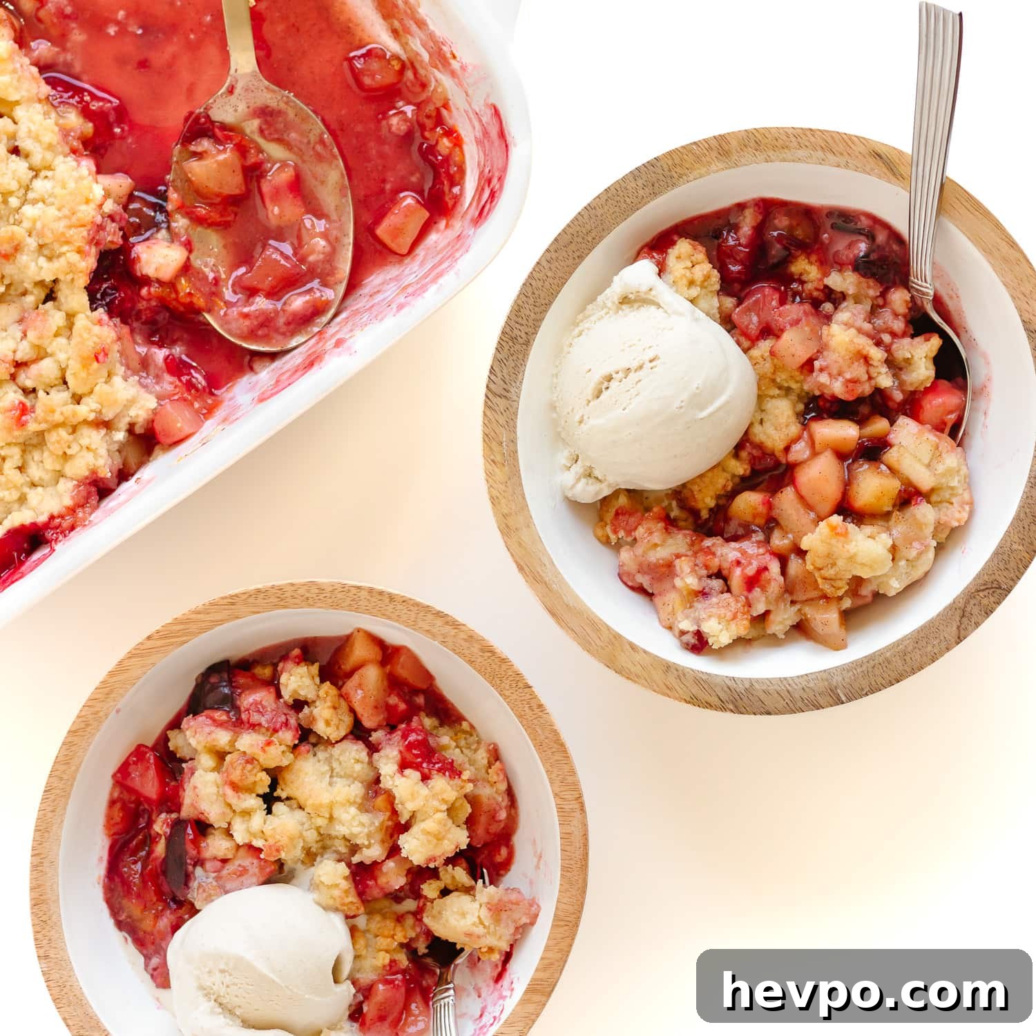 Plum apple crumble being served into two bowls with a scoop of vanilla ice cream.