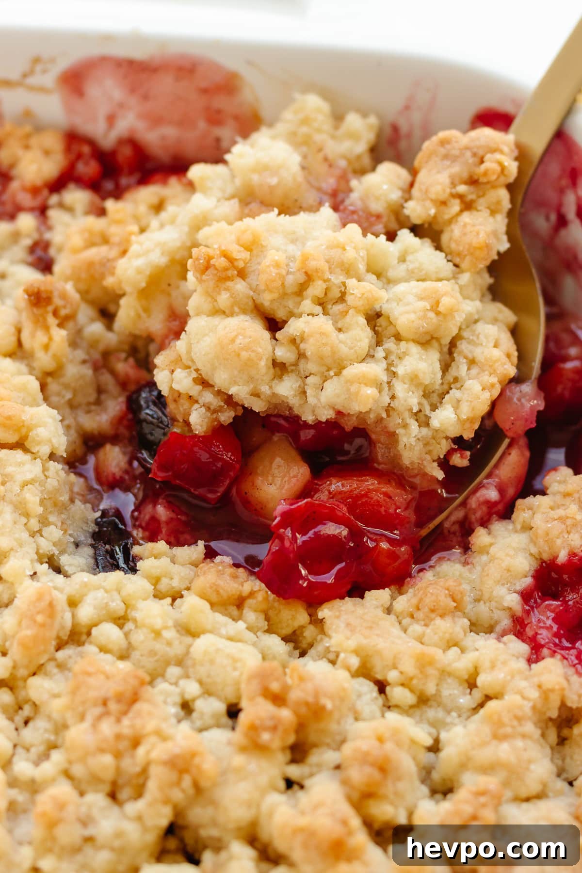 Closeup of a scoop of plum apple crumble being lifted out of baking dish.