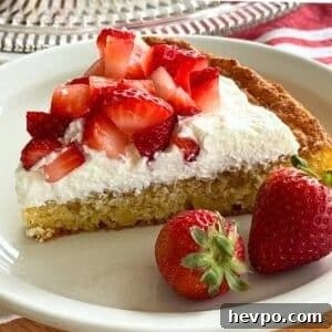 Slice of flourless lemon almond cake topped with whipped cream and strawberries on a white plate.