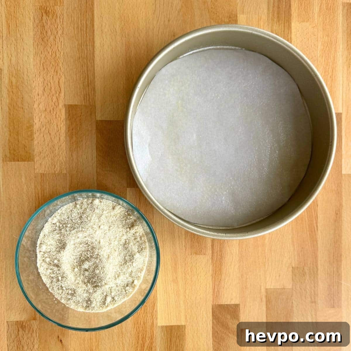 9-inch cake pan with parchment paper in the bottom and glass bowl with almond flour, baking powder, and salt.