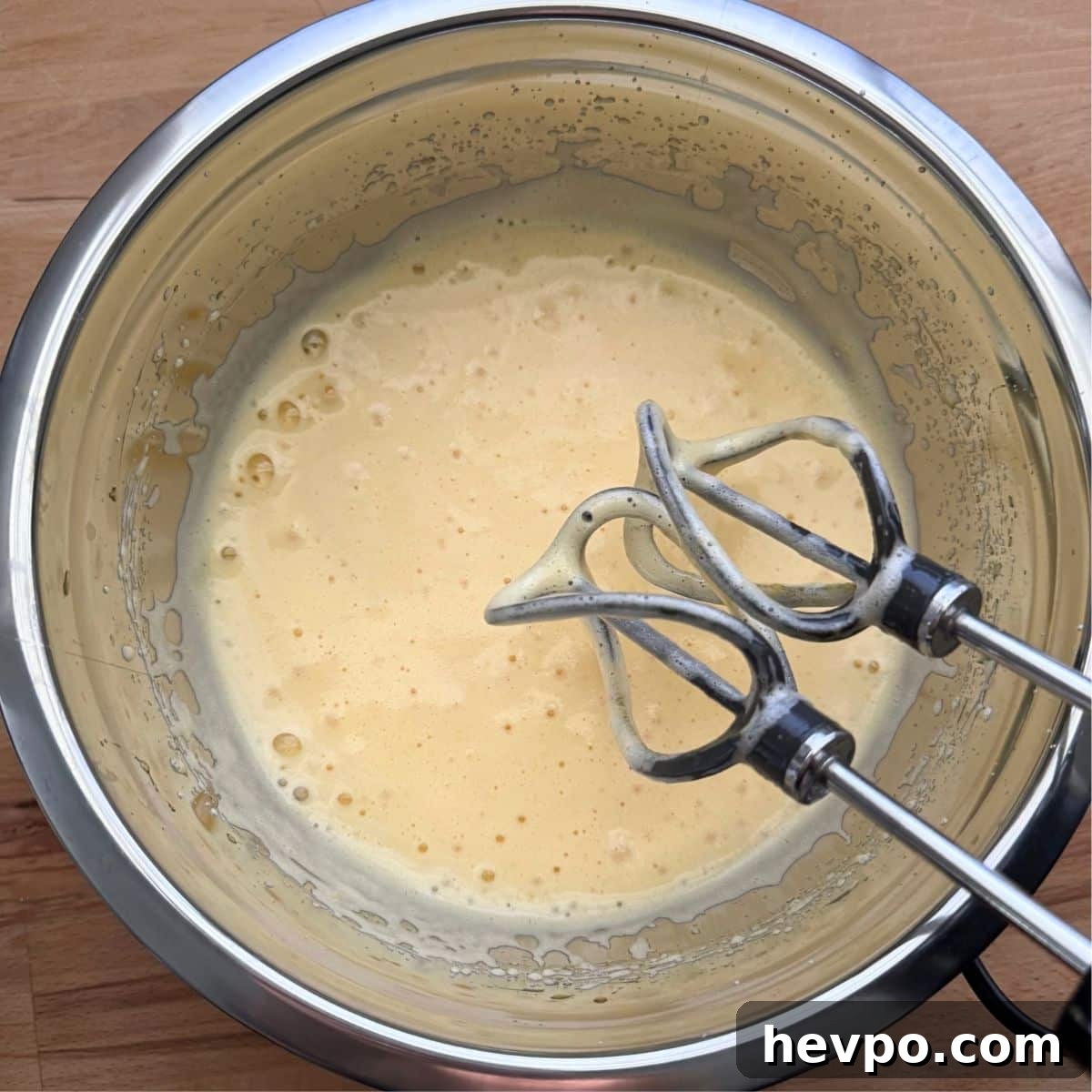 Beaters over whipped eggs and sweetener in a stainless steel bowl with two beaters over it.
