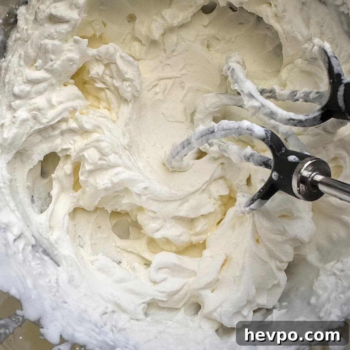 Heavy cream and sweetener whipped in a bowl with beaters inserted.