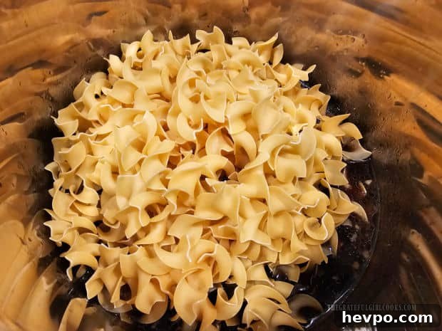 Uncooked egg noodles added and pressed into the broth