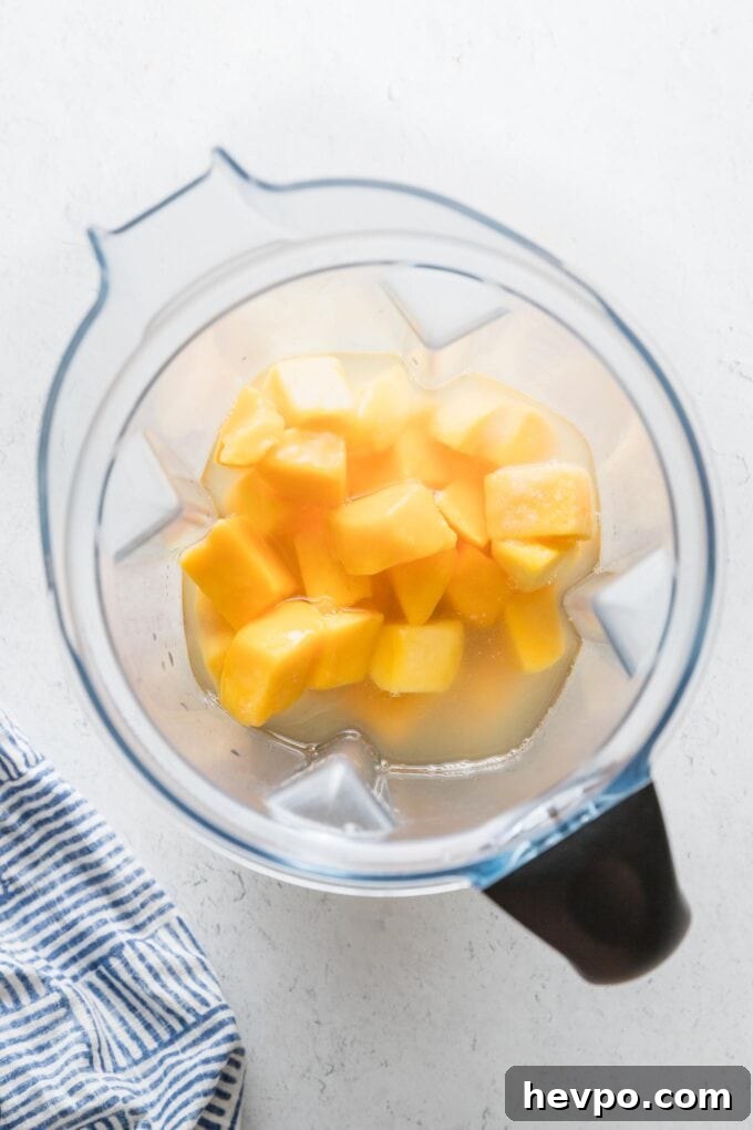 Large blender full of frozen mango chunks, lemon juice, sugar, and water.