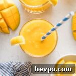 Overhead view of a small glass filled with frozen mango lemonade topped with a lemon wedge and a blue and white striped paper straw.
