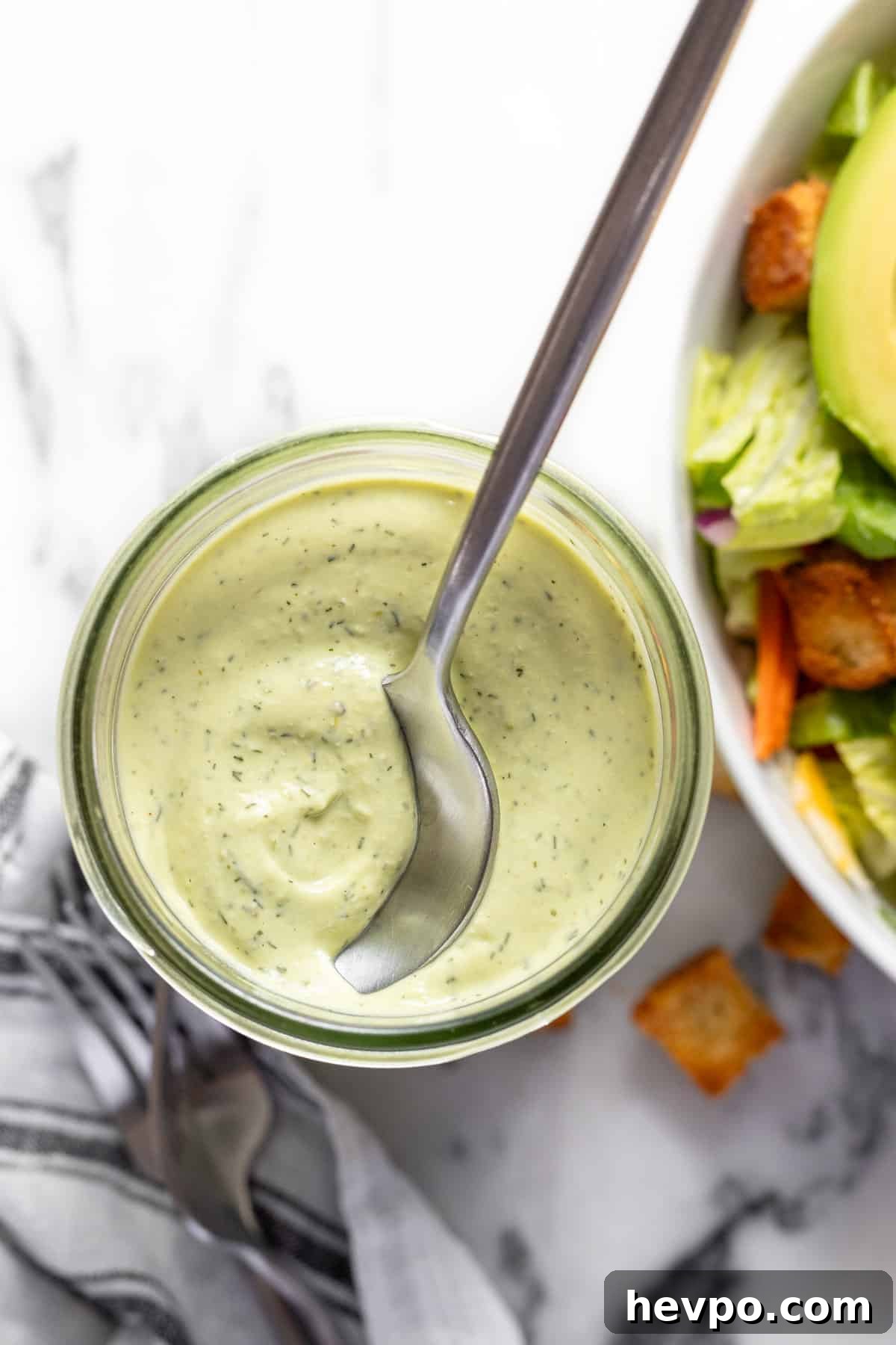 Wide-mouth mason jar filled with creamy avocado lime ranch dressing with a spoon in it.