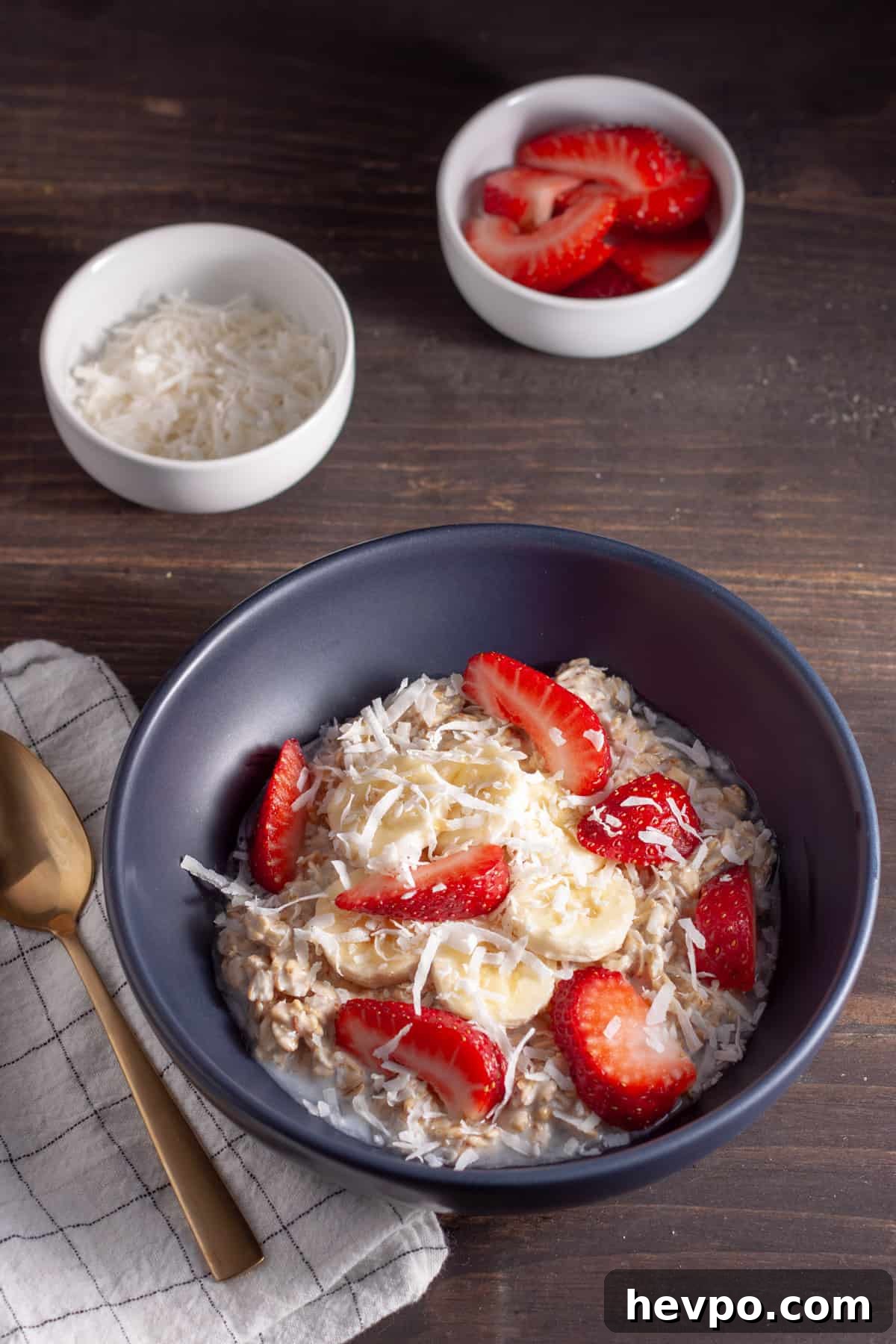 Coconut Milk Overnight Oats Recipe for Creamy Breakfast 6 A bowl of overnight oats made with coconut milk in a blue bowl topped with shredded coconut, berries and banana slices.