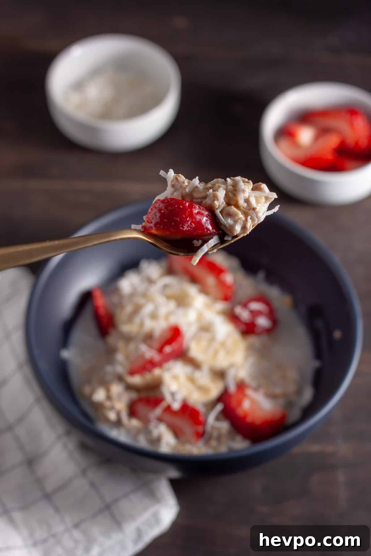 Coconut Milk Overnight Oats Recipe for Creamy Breakfast 8 A spoonful of coconut overnight oats above a bowl of the oats with strawberries, bananas and shredded coconut.