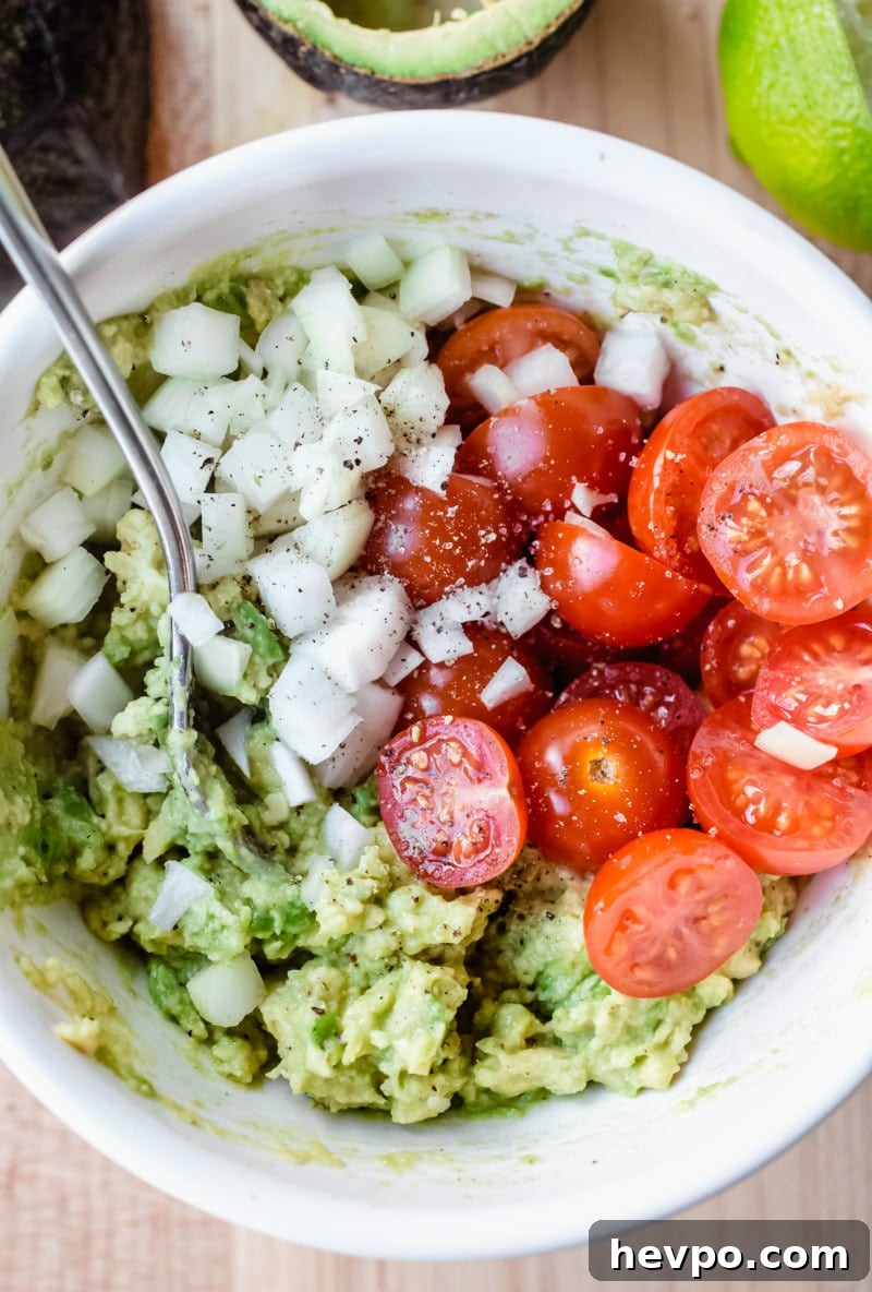 making filling for stuffed avocados (onion, avocado, tomato in a white bowl)
