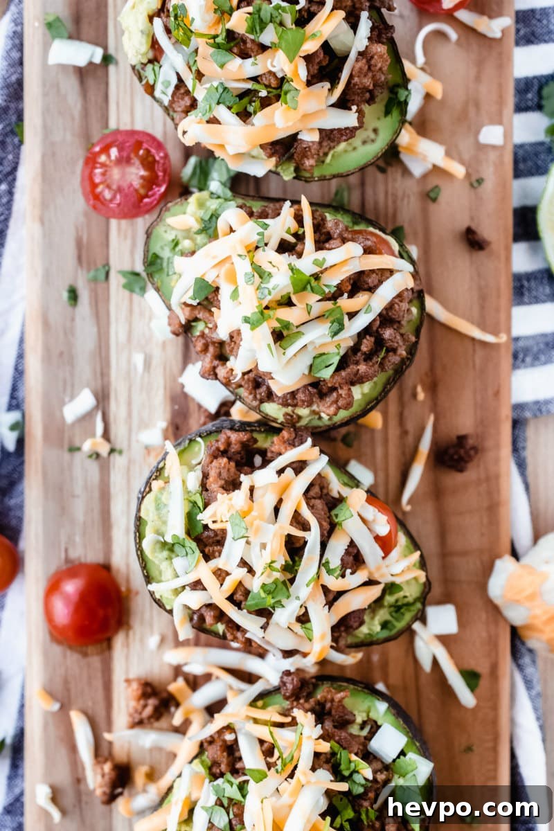 four avocado halves stuffed with taco filling on a wooden cutting board