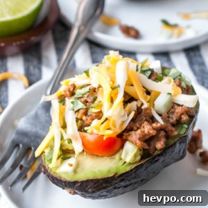 half an avocado stuffed with taco filling. On a white plate with a fork.
