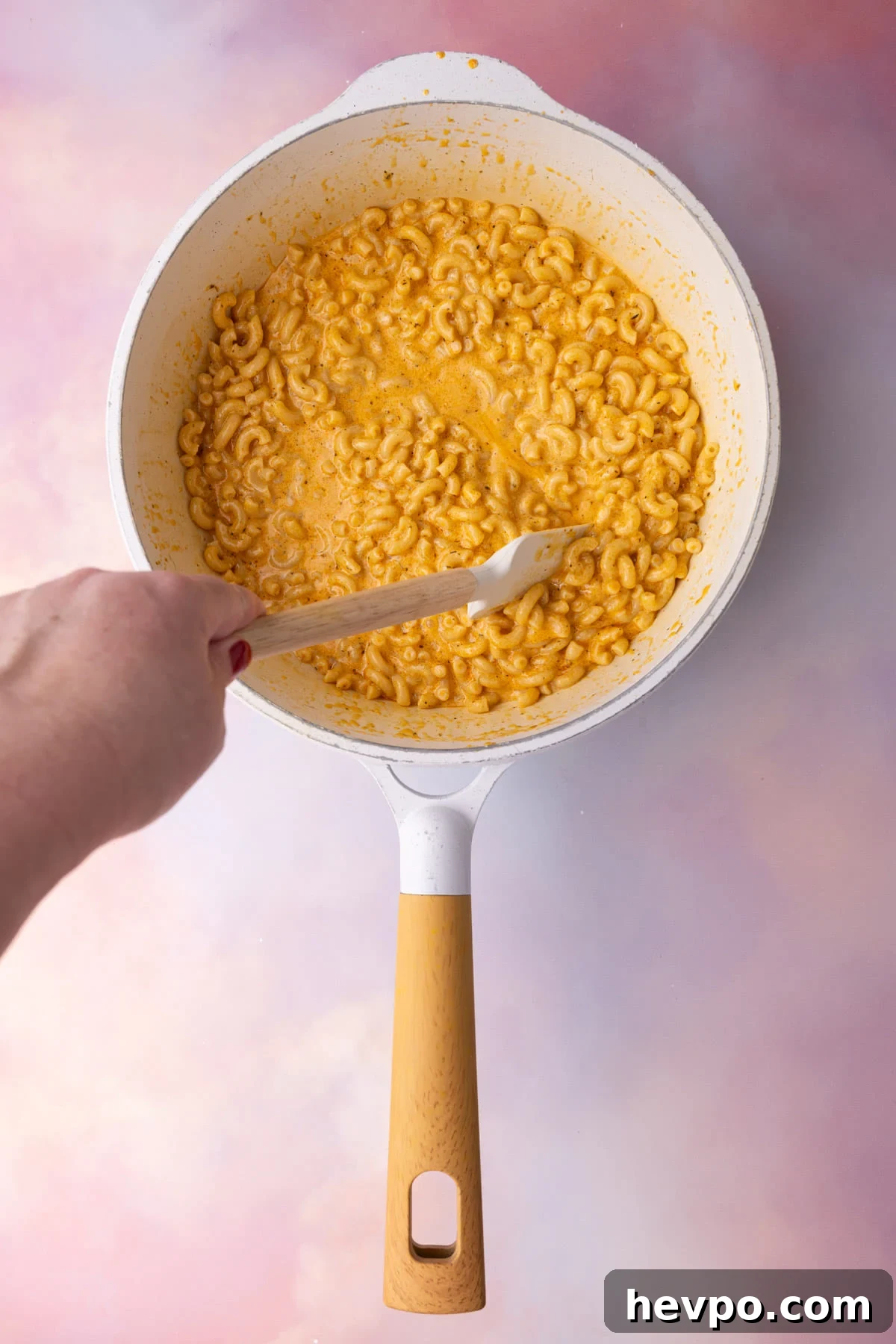 Stirring cooked elbow macaroni into Cajun cheese sauce. 