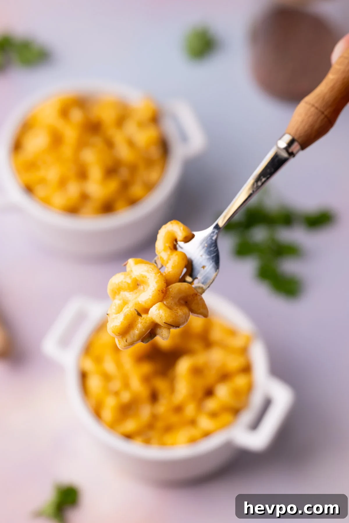 Spicy mac n cheese on a fork with two bowl and Cajun seasoning jar in the background.
