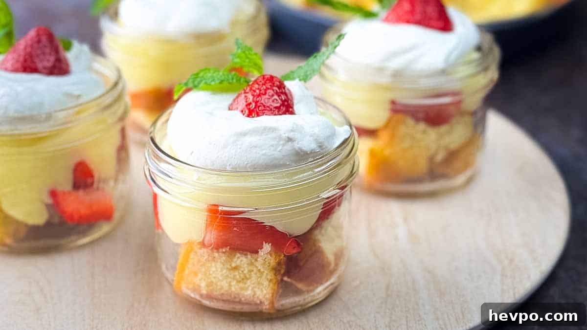 Jars of strawberry shortcake parfaits garnished with strawberries and mint on a serving tray.