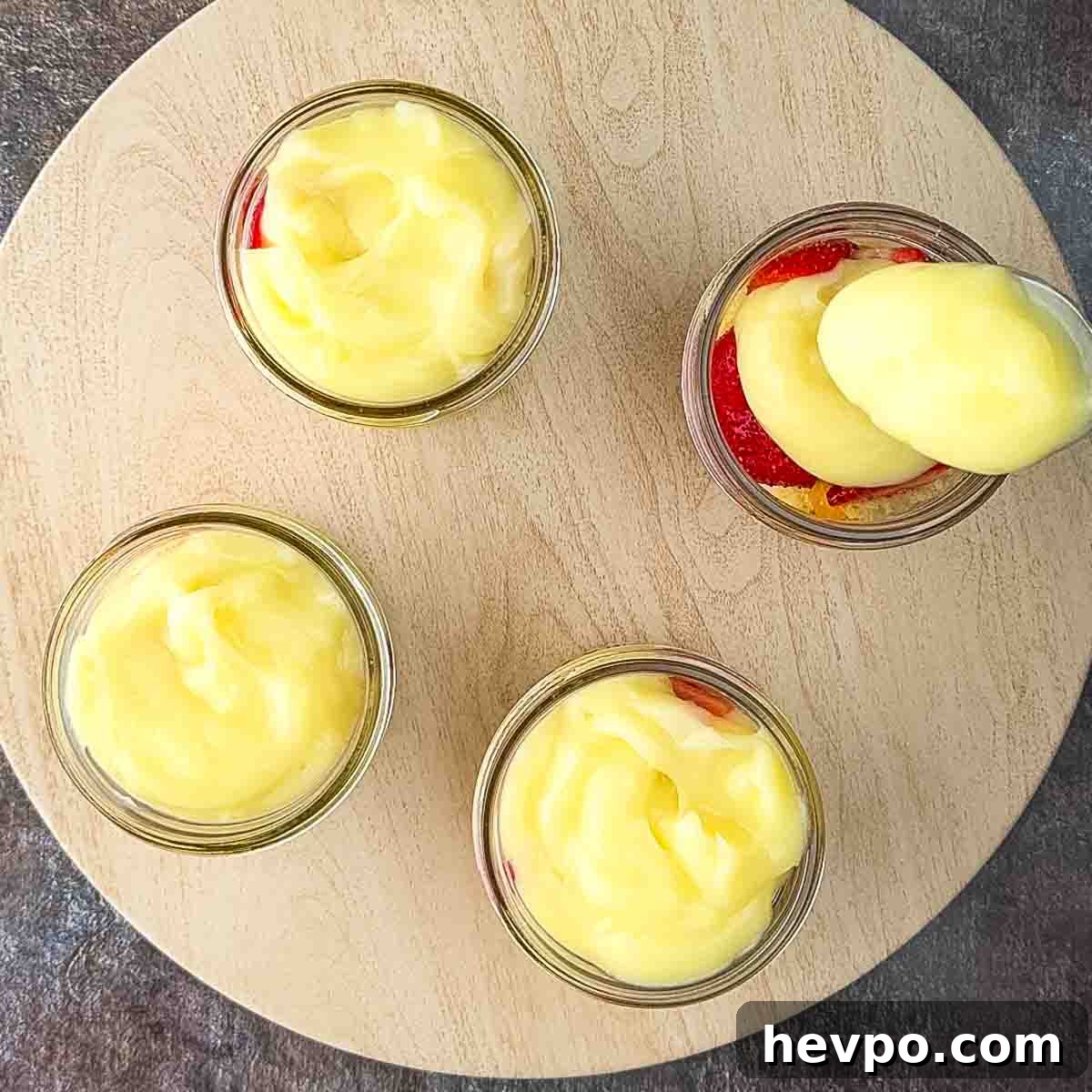 The vanilla pudding being placed on top of the strawberries in jars.
