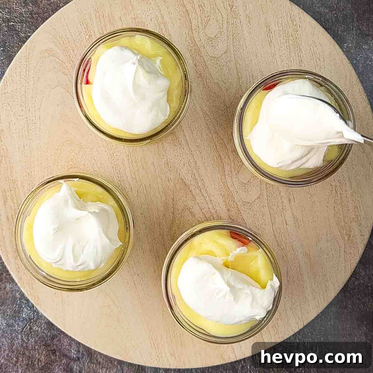 A spoon placing Cool Whip on top of the pudding in jars.