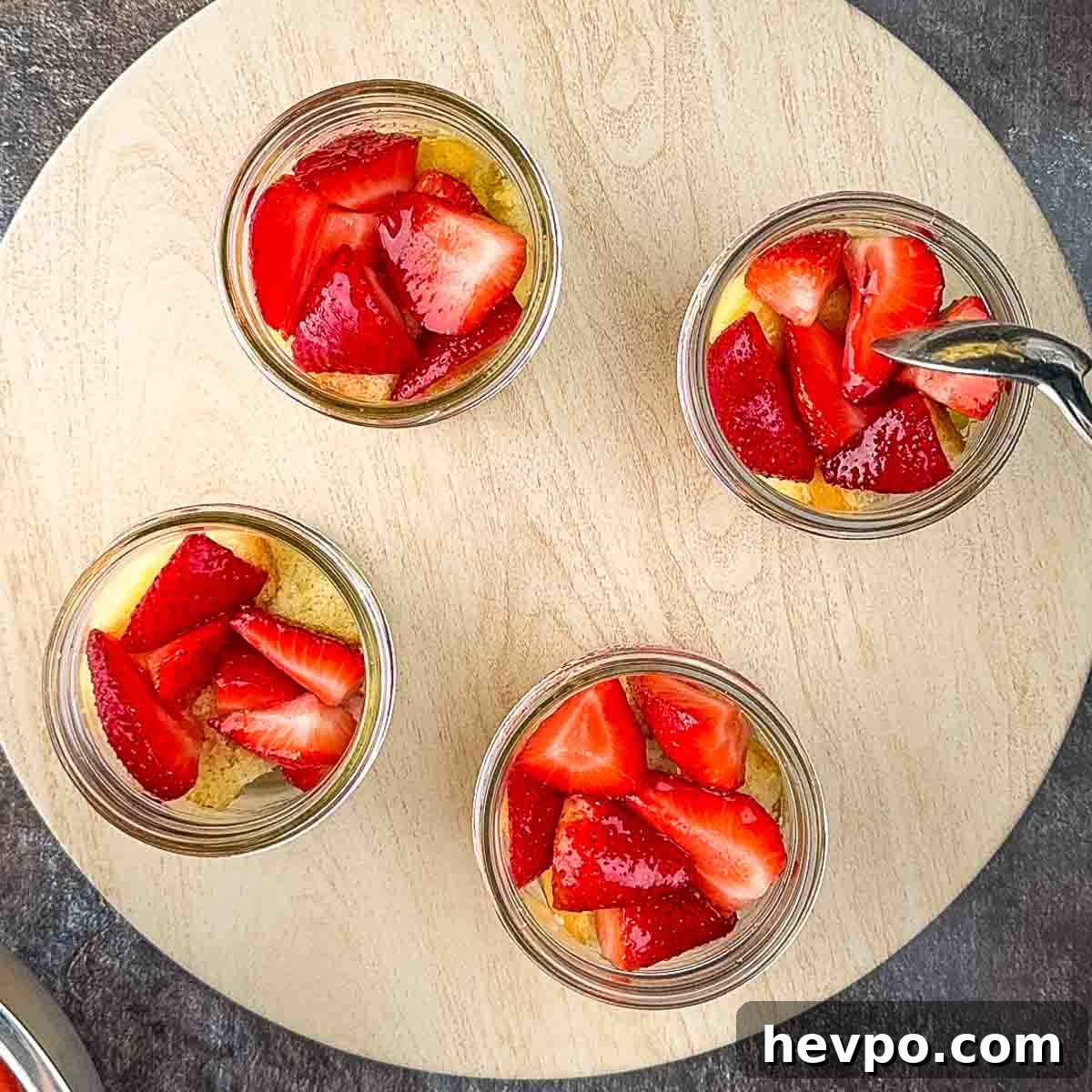 A spoon placing strawberries on top of the cake cubes.