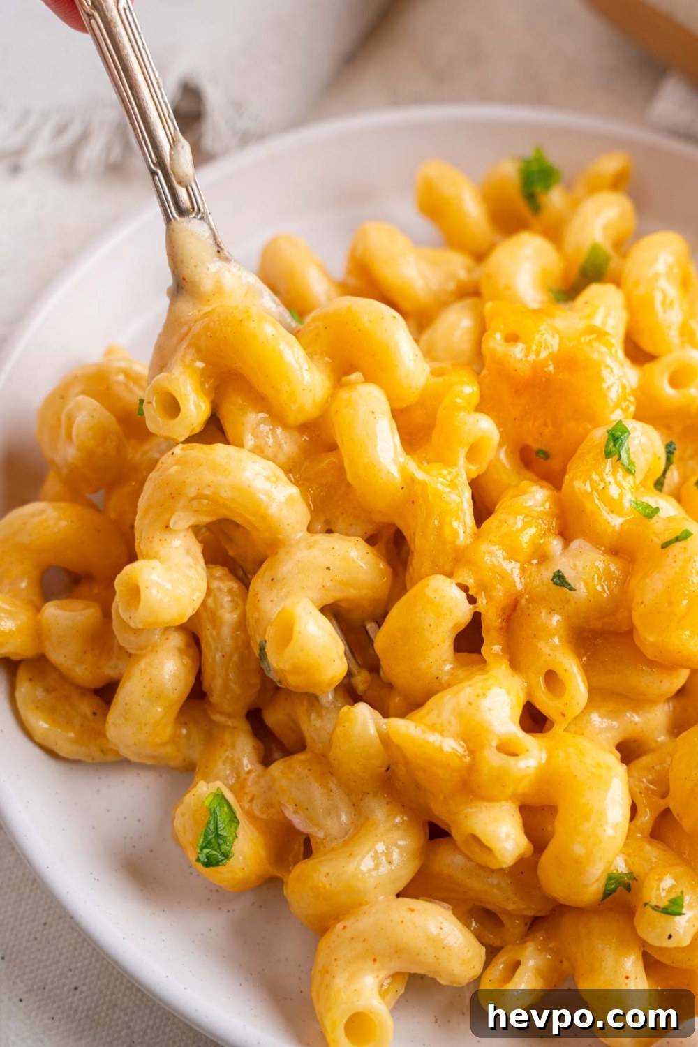 Tini’s Viral TikTok Mac and Cheese Recipe 2 A fork taking a bite of Tini's mac and cheese from a white plate. The plate is on a white counter and garnished with fresh parsley.