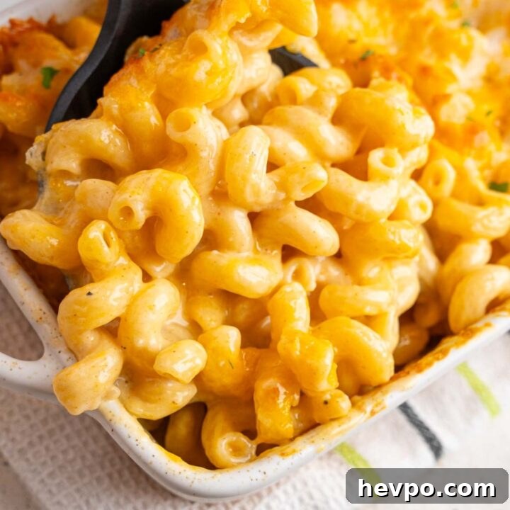 A rubber spatula inserted into a white ceramic baking dish with Tini's mac and cheese. The baking dish is on a kitchen towel on a white counter.