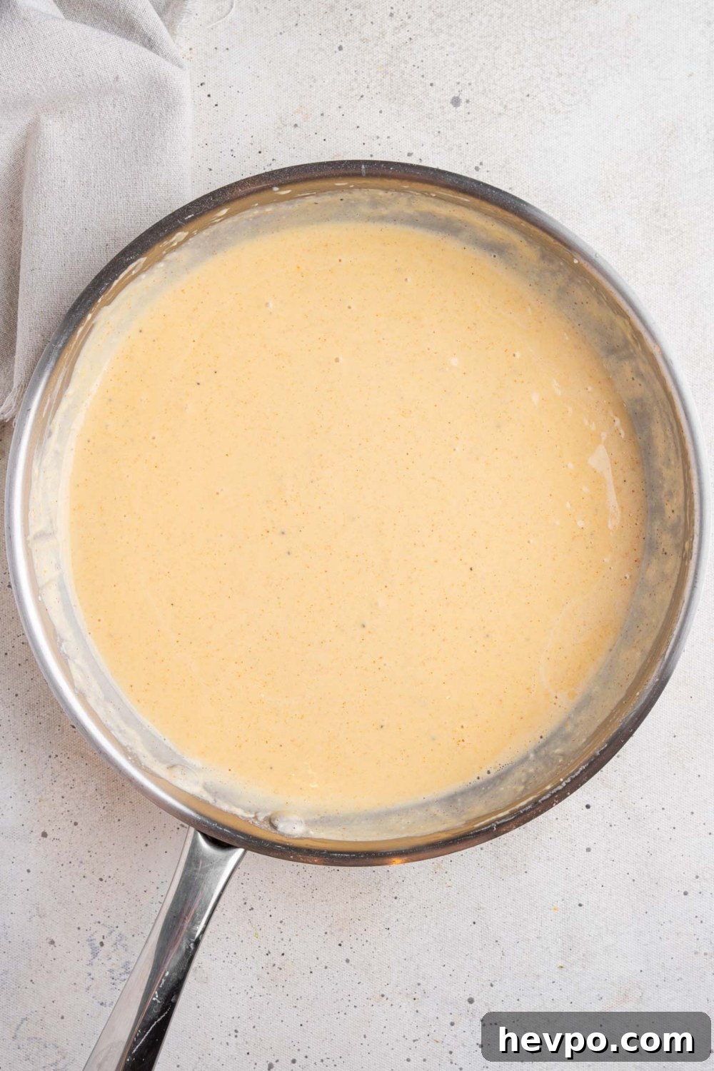 Tini’s Viral TikTok Mac and Cheese Recipe 7 A stainless steel pan with a thickened mac and cheese sauce. The pan is on a white counter with a white cloth napkin.