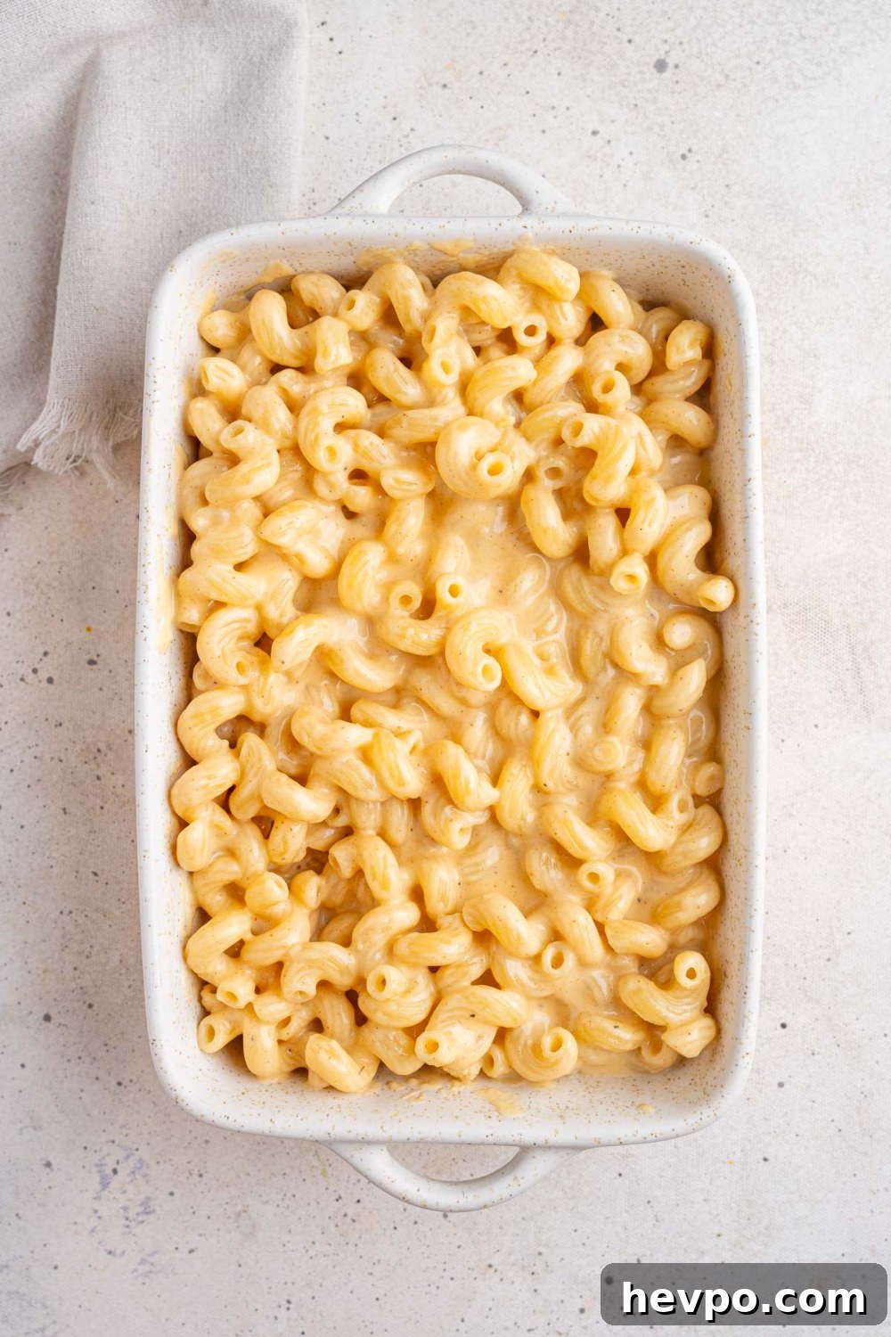 Tini’s Viral TikTok Mac and Cheese Recipe 8 A white ceramic baking dish with macaroni and cheese on the bottom layer. The dish is on a white counter with a white cloth napkin.