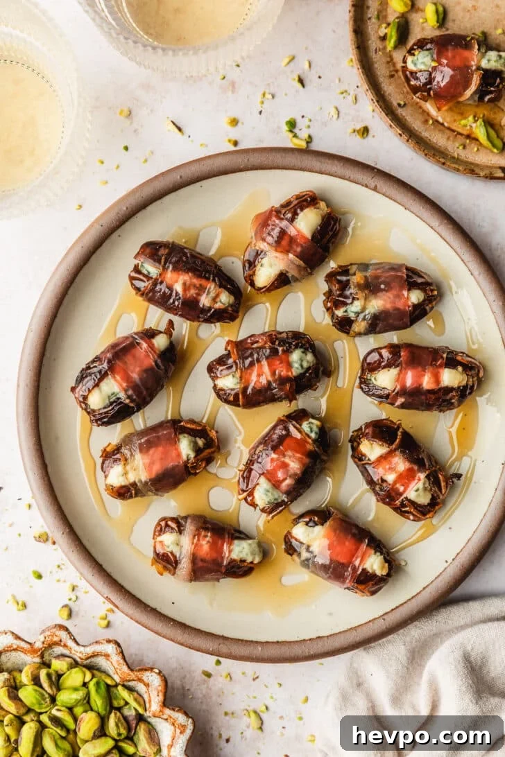 Prosciutto-Wrapped Dates with 3 Simple Ingredients 11 A plate of prosciutto wrapped dates on a tan counter next to a beige linen, glasses of white wine, and brown plates of pistachios and dates.