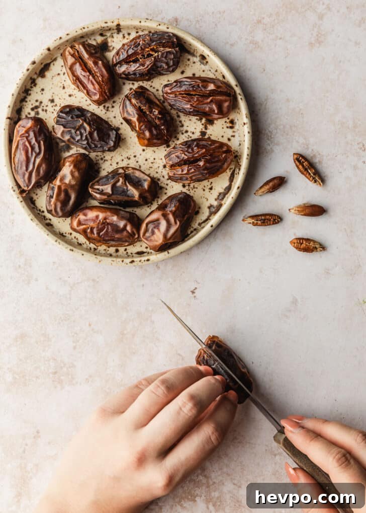 Prosciutto-Wrapped Dates with 3 Simple Ingredients 4 A hand using a knife to slice open a date on a tan counter next to a brown plate of dates.