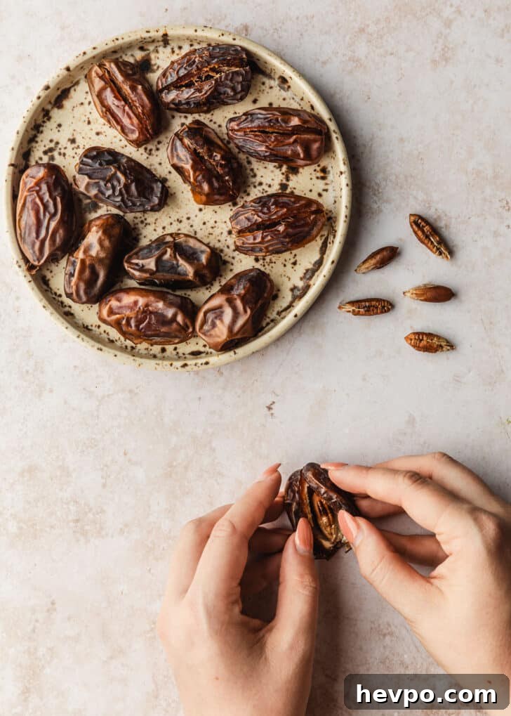 Prosciutto-Wrapped Dates with 3 Simple Ingredients 5 Hands opening up a date on a tan counter next to a brown plate of dates.