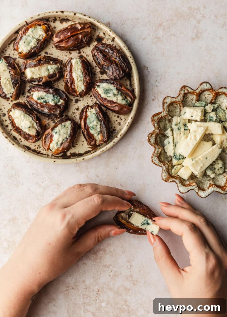 Prosciutto-Wrapped Dates with 3 Simple Ingredients 7 Hands placing a wedge of blue cheese into a date next to brown bowls of dates and blue cheese on a tan counter.