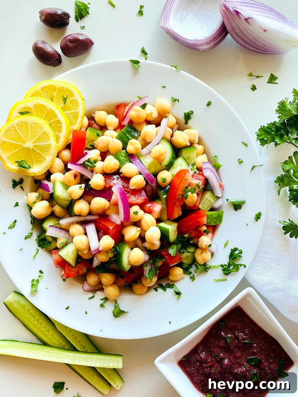 Mediterranean chickpea salad in a white bowl next to a dish of kalamata dressing