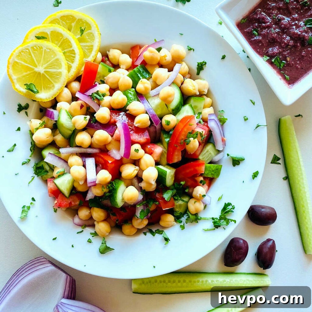 Mediterranean chickpea salad in a white bowl next to a dish of kalamata dressing