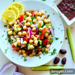 Mediterranean chickpea salad in a white bowl next to a dish of kalamata dressing