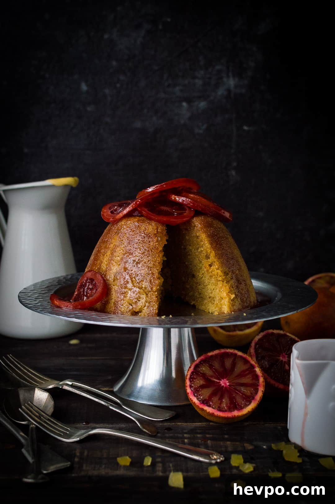 Sliced blood orange and ginger steamed pudding topped with candied blood orange slices on a silver cake stand