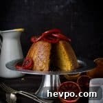 Sliced blood orange and ginger steamed pudding topped with candied blood orange slices on a silver cake stand