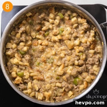 Bread cubes and chicken broth combined with sausage and vegetables in a saucepan.