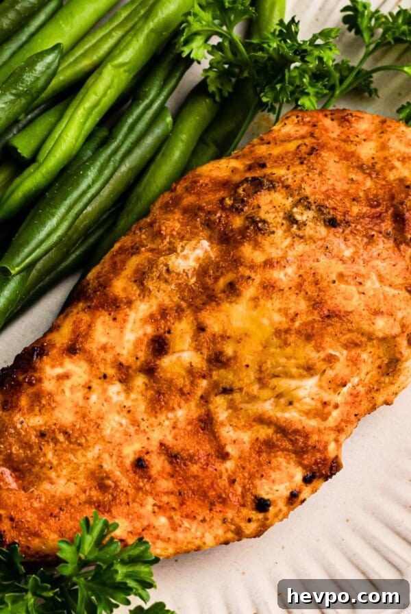 Golden, air fried chicken on a white plate with green beans.