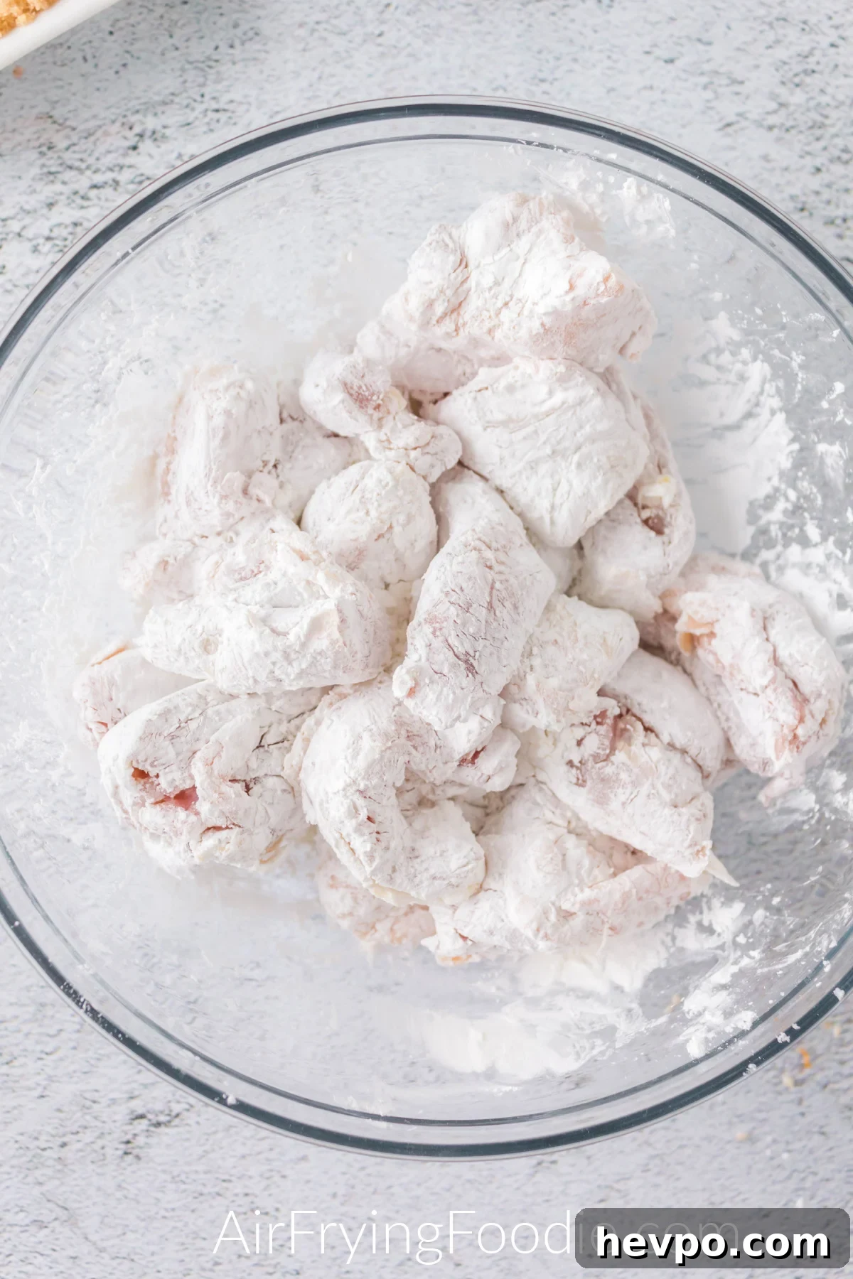 chicken tossed in cornstarch and flour in a glass bowl.