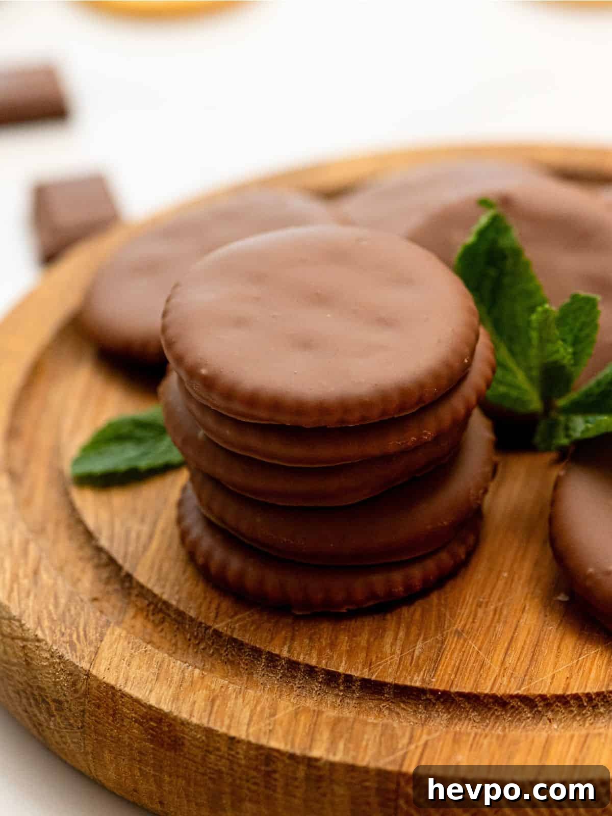 Stack of homemade thin mint cookies on a wooden cutting board with fresh mint leaves