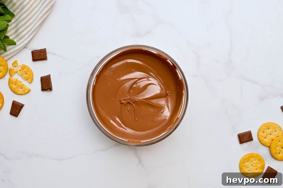 Melted chocolate for thin mint cookies in a glass bowl with crackers nearby