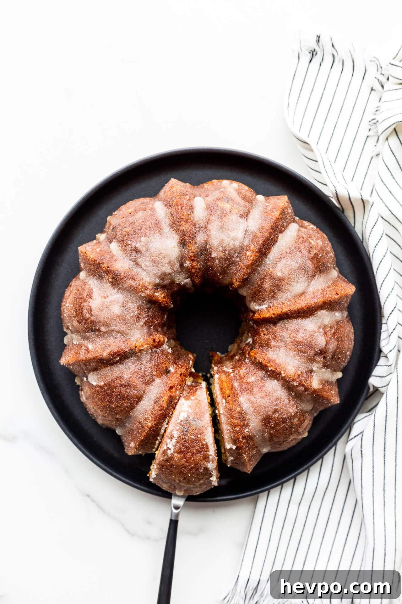 Glazed bundt cake with slice cut, on a black plate.