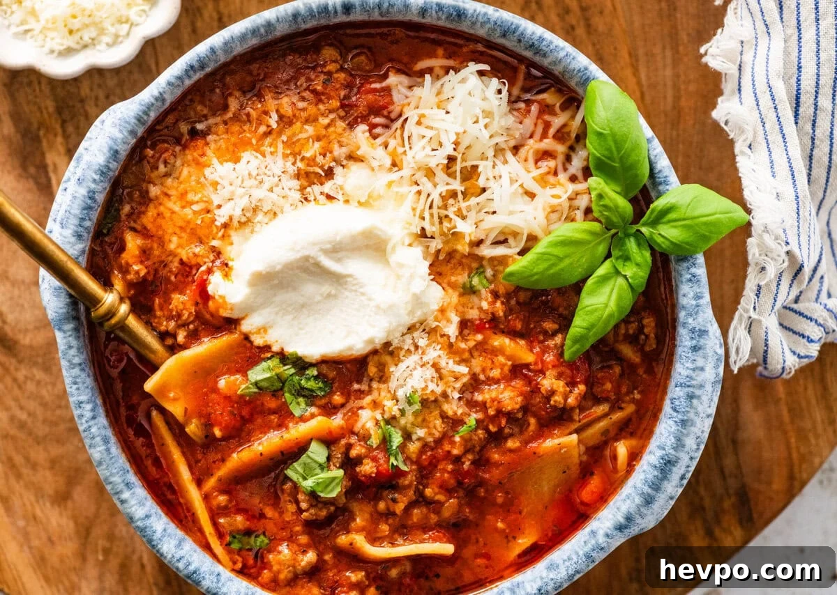 lasagna soup in a bowl topped with basil and cheese with more toppings in the background.